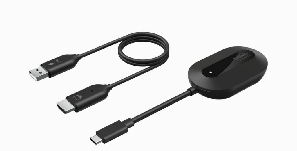 A imagem apresenta o Belkin ConnectAir, um adaptador de ecrã HDMI sem fios, composto por dois componentes principais em preto mate. Do lado esquerdo, vê-se um cabo em "Y" que serve para a receção e alimentação. Numa extremidade, possui uma ficha USB-A (identificada com um ícone de raio e a indicação de 2.3W) para ligar a uma fonte de energia. A outra extremidade termina numa ficha HDMI, que se liga à televisão ou monitor, apresentando um ícone de um ecrã com uma bateria. Do lado direito, destaca-se a unidade principal, um dongle de formato oval com um acabamento elegante. A face superior tem uma secção em plástico brilhante onde se lê a marca "belkin" e o modelo "ConnectAir", incluindo ainda uma pequena luz LED indicadora de estado. Desta unidade sai um cabo curto que termina num conetor USB-C, destinado a ser ligado ao dispositivo de origem (como um portátil, tablet ou smartphone) para transmitir o sinal de vídeo sem fios para o recetor ligado à televisão.