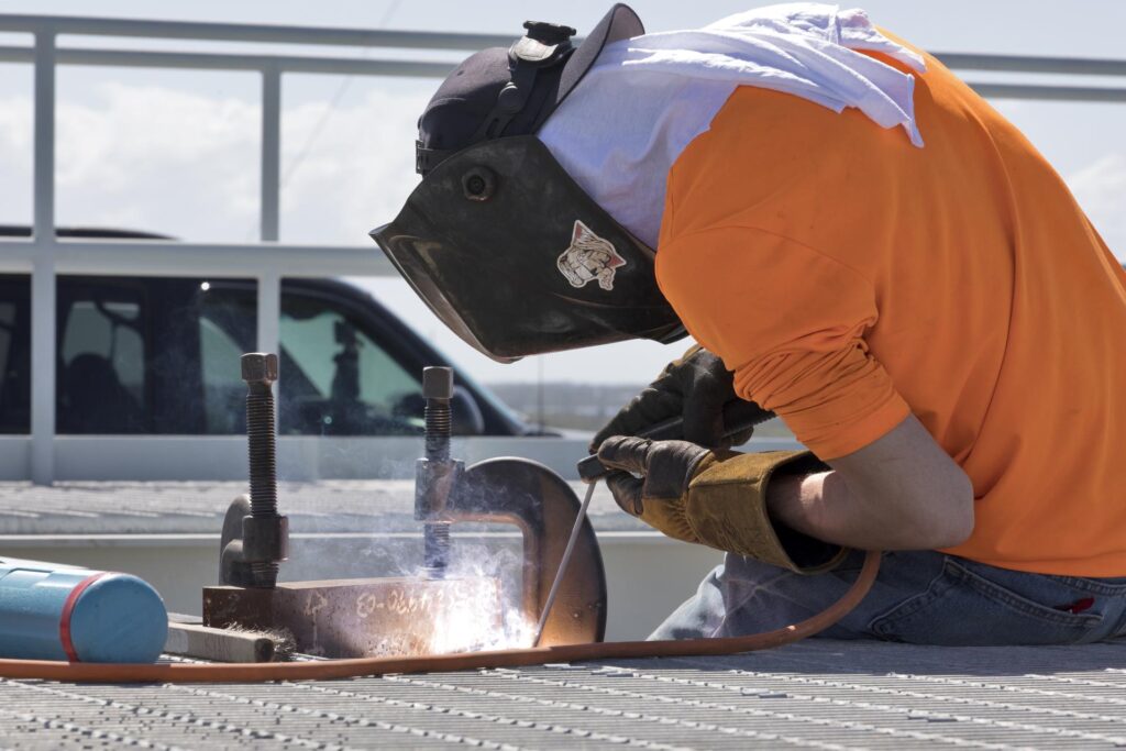 Trabalhador com máscara de proteção a soldar uma estrutura metálica na plataforma de lançamento, com faíscas brilhantes a saltar do metal.