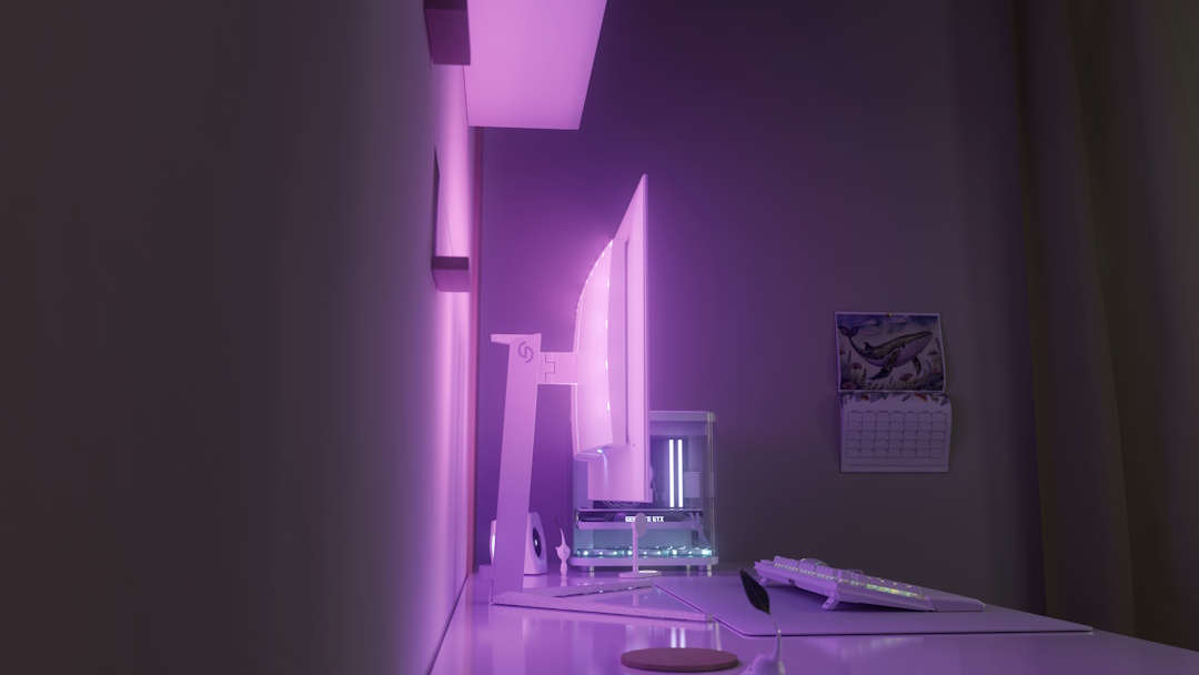 Fotografia lateral de um setup gaming minimalista predominantemente branco num ambiente de pouca luz. No centro, um monitor visto de perfil projeta uma intensa luz ambiente roxa e rosa na parede através de LEDs traseiros. A secretária inclui um teclado, um tapete de rato largo e uma torre de PC envidraçada com luzes claras ao fundo. Na parede lateral direita, está pendurado um calendário com o desenho de uma baleia.