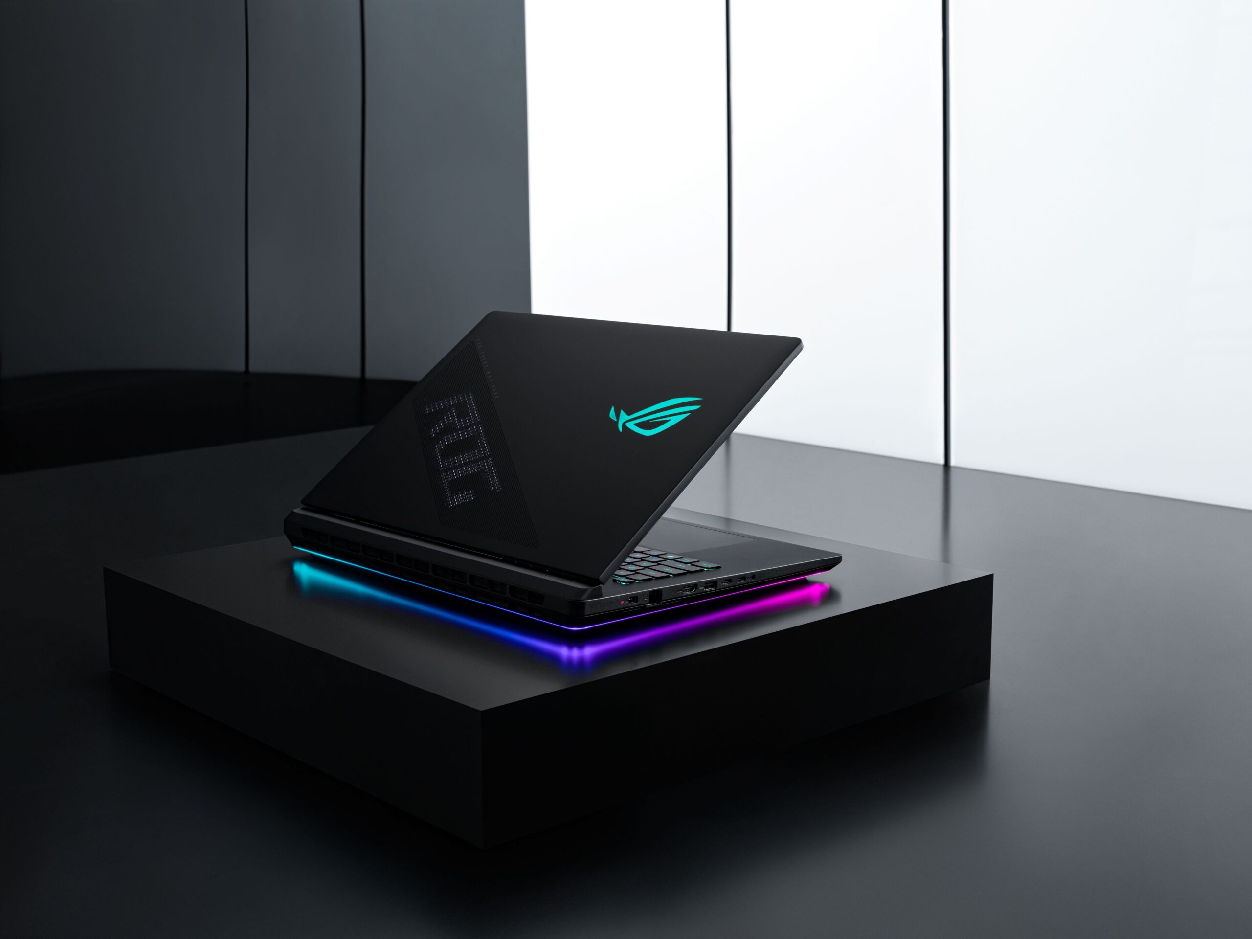 Portátil gaming ROG Strix SCAR 18 preto, semiaberto sobre um pedestal escuro, com iluminação RGB na base e logótipo brilhante a ciano na tampa.