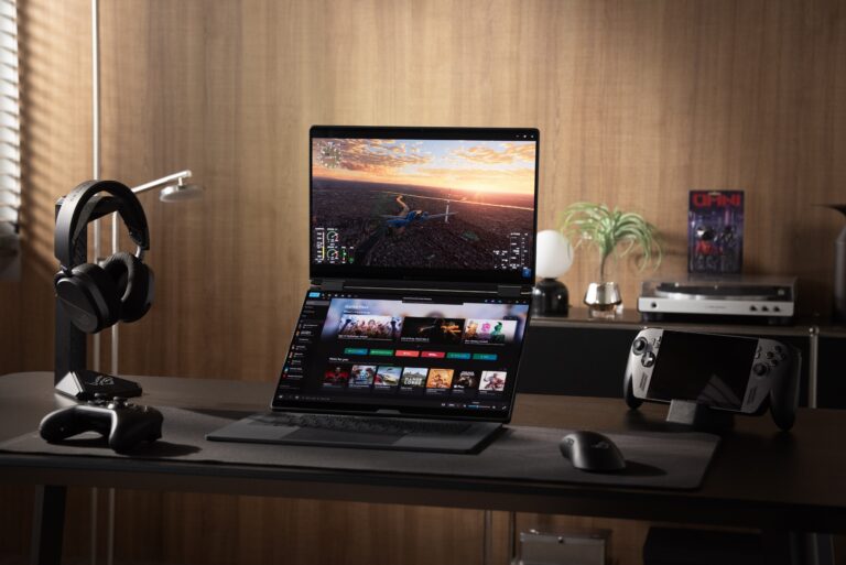 Fotografia de um setup gaming requintado numa secretária. No centro está o portátil ROG Zephyrus Duo com os seus dois ecrãs iluminados, rodeado por auscultadores num suporte, um comando, um rato e uma consola portátil ROG Ally. O fundo tem uma parede de madeira acolhedora com decoração subtil e iluminação quente.