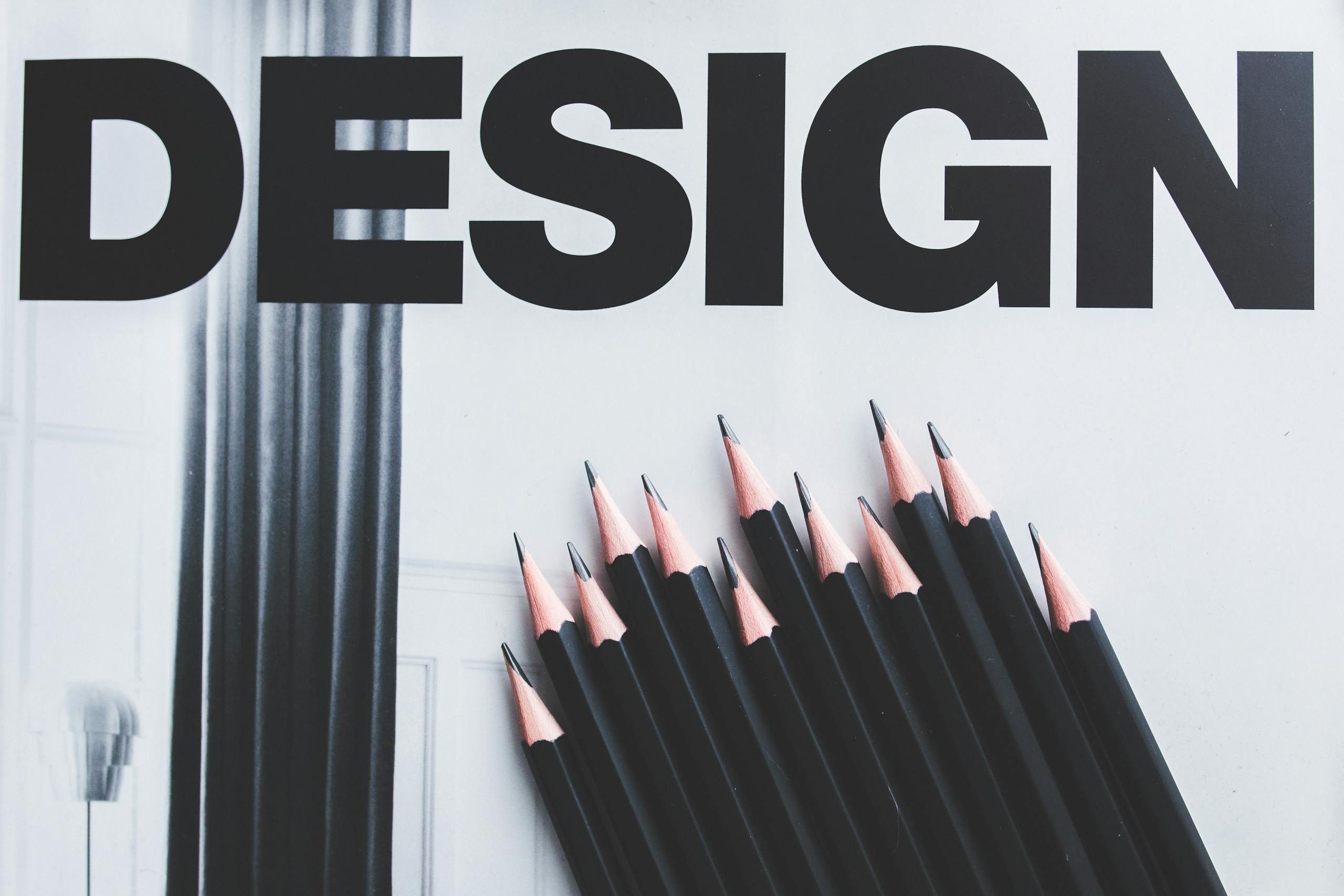 Black pencils arranged creatively next to large typography 'DESIGN'.